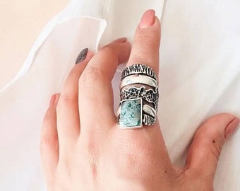 Puede incluir: Un anillo de plata con una piedra verde engastada en una banda texturizada. El anillo está apilado con otras bandas de plata.