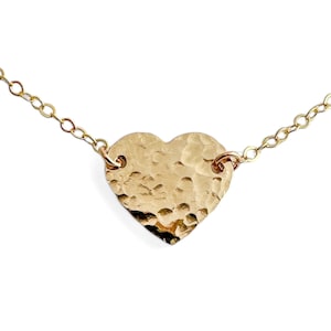 May include: A gold heart-shaped pendant necklace with a hammered texture. The chain is delicate and made of gold.
