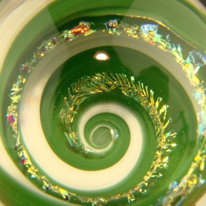 May include: A green glass paperweight with a white spiral design and gold flecks. The paperweight is clear and has a shiny finish.