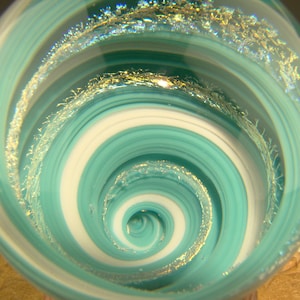 May include: A glass paperweight with a swirling pattern of teal and white, accented with gold glitter.