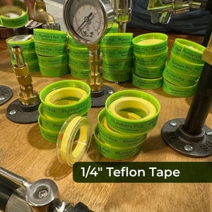 May include: A close-up of a roll of 1/4 inch yellow PTFE tape with green packaging that says "Plumbers Pick 100% Waterproof Teflon Tape".