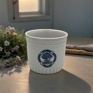 May include: White ceramic cup with a blue and white logo that reads "Confituries Mire Andrée Patelles Fruits Traméries M.C."