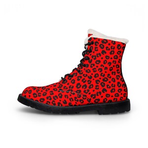 May include: A red combat boot with a black leopard print pattern. The boot has black laces, a black sole, and a white faux fur lining around the top. The boot is designed for cold weather.