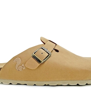 Könnte beinhalten: Tanfarbener Lederclog mit Schnallenverschluss und einem gestickten Eichhörnchen an der Seite. Der Clog hat ein Korkfußbett und eine weiße Gummisohle.