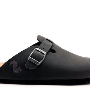 May include: Black leather clog with a buckle closure and a cork footbed. The clog has a squirrel logo on the side.