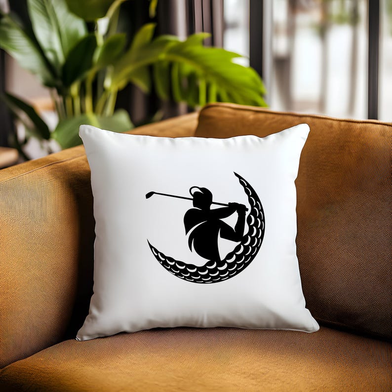 May include: White pillow with a black silhouette of a golfer swinging a club inside a crescent moon shape made of golf balls.