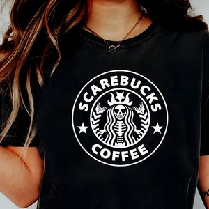 May include: A black t-shirt with a white graphic of a skeleton mermaid with a crown and the text "SCAREBUCKS COFFEE".