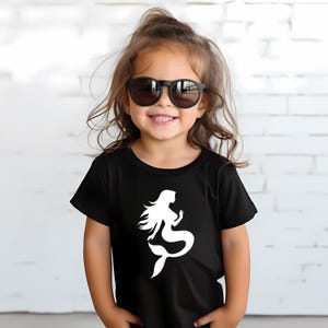 May include: A black t-shirt featuring a white mermaid graphic. The shirt is short-sleeved and appears to be made of a soft material. The image shows a young child wearing the shirt and sunglasses.