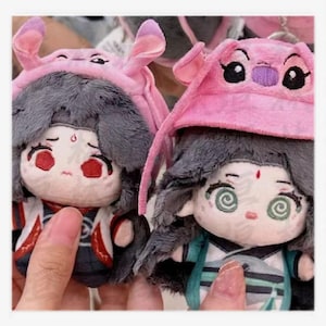 May include: Two plush dolls with gray hair and pink hats resembling a cartoon character. The dolls have detailed facial features, including large eyes and red accents. One doll has red eyes, and the other has spiral eyes. The dolls are wearing detailed outfits.