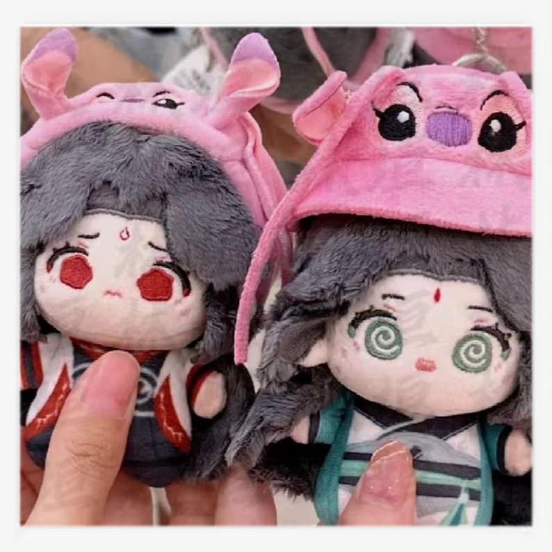 May include: Two plush dolls with gray hair and pink hats resembling a cartoon character. The dolls have detailed facial features, including large eyes and red accents. One doll has red eyes, and the other has spiral eyes. The dolls are wearing detailed outfits.
