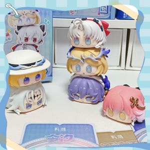 May include: A collection of chibi-style figurines with large eyes and various hair colors, including white, yellow, and pink. Some figurines are stacked, and others are displayed individually. The figurines have a cartoonish aesthetic.