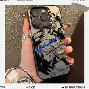 May include: A clear phone case with a black and white anime-style illustration of a character with blue accents. The case has a black border and the text "SO COOL". The phone case is held by a person with long, manicured nails.