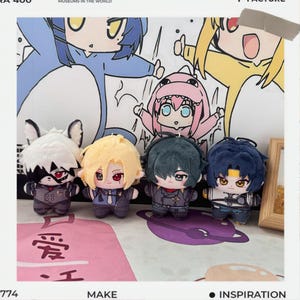 Op de afbeelding: Vier kleine pluche poppen met anime-achtige karakterontwerpen. Elke pop heeft een unieke haarstijl en outfit, met gedetailleerde gelaatstrekken. De poppen zijn gerangschikt in een rij tegen een achtergrond van cartoonillustraties.