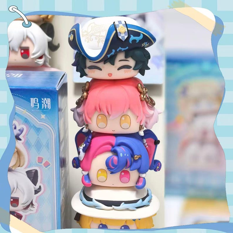 May include: A stack of colorful, cartoon-style figurines. The top figure wears a white and blue hat. The middle figure has pink hair and gold accents. The bottom figure is split between pink and blue. A box with Chinese text is visible.