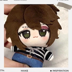 May include: A plush doll with brown hair and green eyes, wearing a black and white striped shirt and blue jeans. The doll has a small, smiling face and a pink blush. The doll is held by a person.