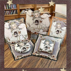 Può includere: Una collezione di stampe artistiche e spille con un'illustrazione stravagante di una ragazza in un vestito con pecore e la parola "memory". La tavolozza dei colori comprende bianco, marrone e nero.