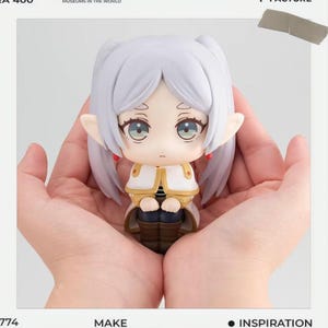 Puede incluir: Una pequeña figura de un personaje con cabello blanco, orejas grandes y un atuendo detallado. La figura se sostiene en manos abiertas sobre un fondo blanco. La figura tiene ojos grandes y viste un atuendo blanco y dorado.