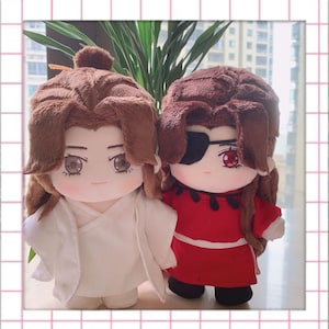 May include: Two plush dolls with brown hair and detailed facial features. One doll wears a white outfit, the other a red outfit with a black eyepatch. Both dolls have a soft, plush texture and are designed with large eyes.
