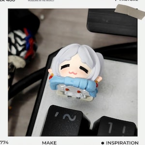 May include: A light blue and white anime-style figurine with a bow, resting on a keyboard. The figurine has a smiling face and is wearing a blue scarf. The keyboard keys are black. The image includes the words "MAKE" and "INSPIRATION".