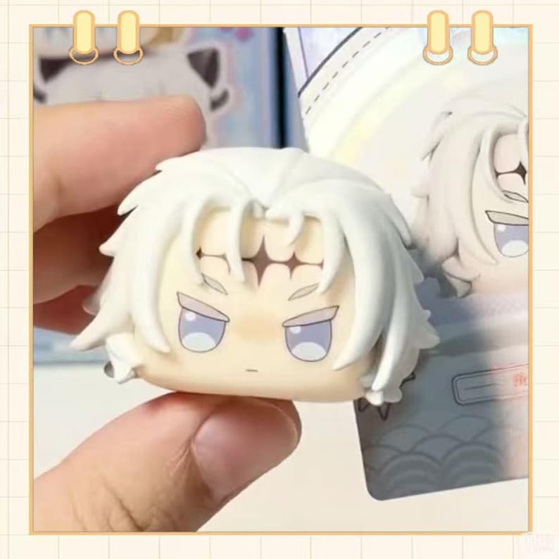 May include: A small, white figurine head with spiky hair and a stern expression. The figurine has light blue eyes and a neutral skin tone. The head is held in a hand, with a blurred background showing similar figurines.