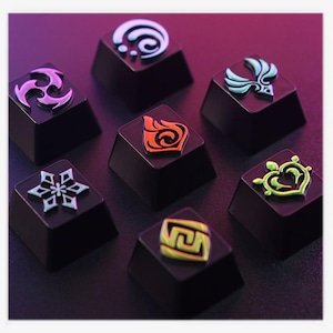 May include: Seven black keycaps with colorful, raised symbols. The symbols include a white swirl, a purple and white design, a teal and white emblem, a red and orange flame, a white snowflake, a green heart, and a yellow and green design.