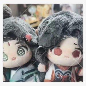 May include: Two plush dolls with gray fur-like hair and embroidered facial features. The dolls have detailed clothing with red and blue accents. One doll has a red accent on its hair, and both have spiral designs on their eyes.