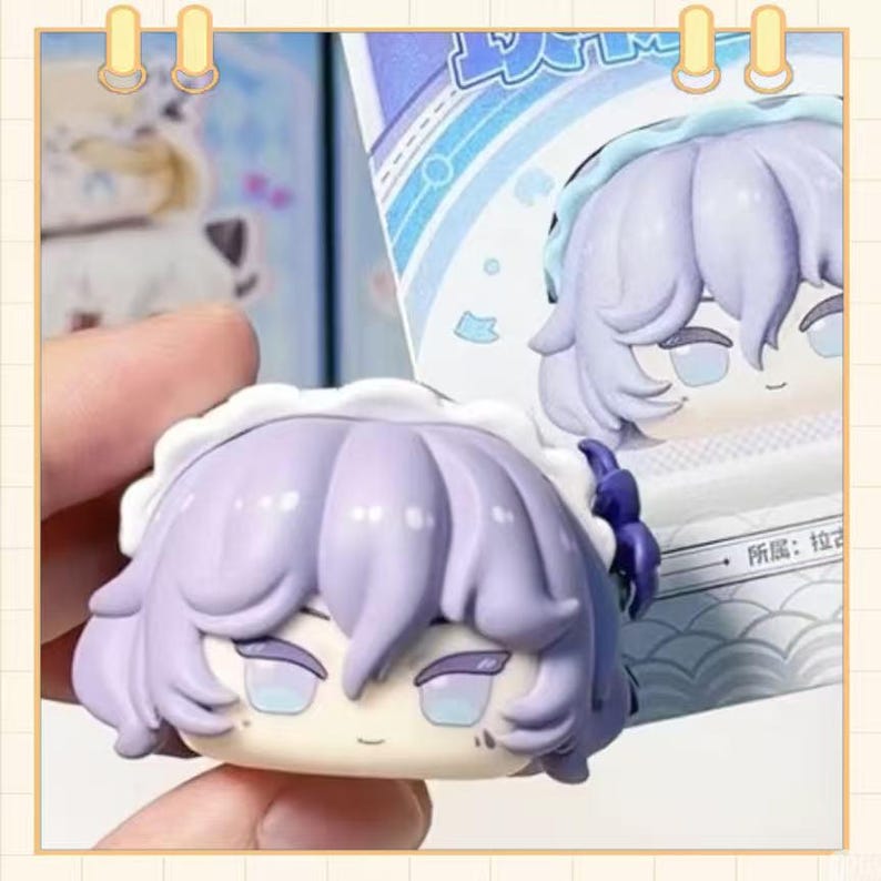 May include: A close-up of a small, collectible figurine with a stylized anime aesthetic. The figure has lavender hair, a white frilly cap, and a serene expression. The figure is held in a hand, with a portion of the packaging visible in the background.