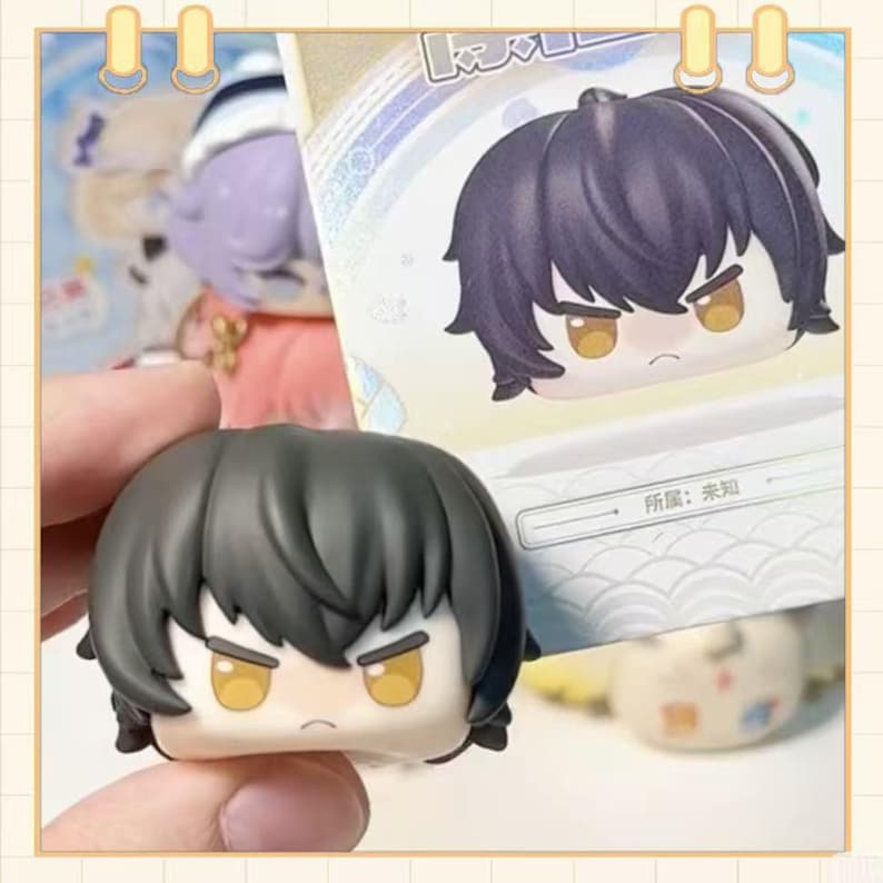 May include: A small, black-haired figurine with a stern expression and yellow eyes is held in a hand. The figurine is a miniature version of a character from a cartoon or anime. A card with a matching illustration is behind it.