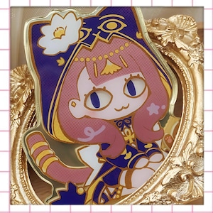 Könnte beinhalten: Ein goldfarbener, gerahmter Anstecker mit einer cartoonartigen, katzenartigen Figur mit rosa Haaren und blauen Augen. Die Figur trägt ein blaues und goldenes Outfit mit einer weißen Blume auf dem Kopf. Der Anstecker ist in einem goldfarbenen, verzierten Rahmen angebracht.