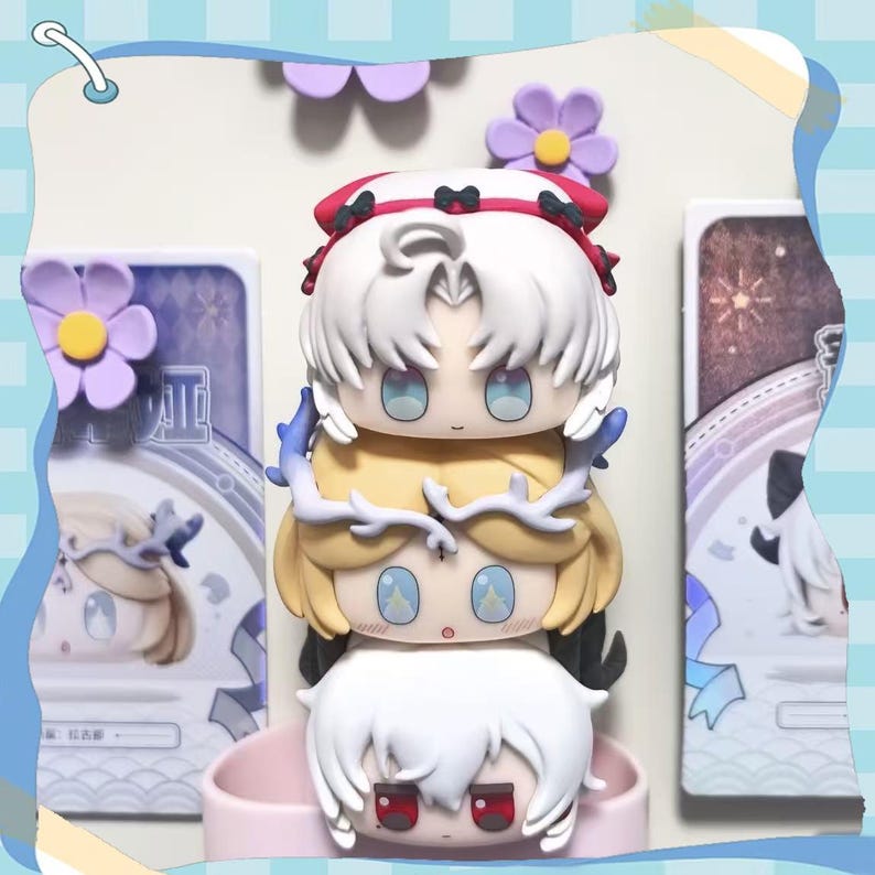 May include: A stack of four chibi-style figures with white, yellow, and red hair, and blue eyes. The figures are stacked on top of each other, with a pink base. The background includes decorative elements and a light blue border.
