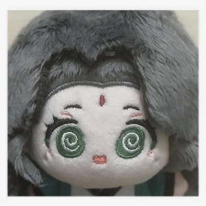 May include: A plush doll with a white face, green spiral eyes, and a small red mark on the forehead. The doll has gray, fluffy hair and a small, embroidered pink mouth. The doll is wearing a green and white outfit.