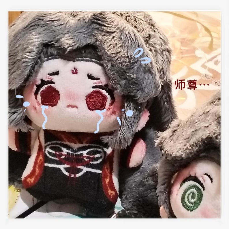 May include: A plush doll with a sad expression, tears, and a gray fur hat. The doll has red eyes and a detailed outfit with red and black accents. The text "师尊..." is visible in the image.
