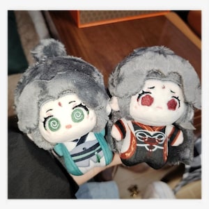 May include: Two plush dolls with gray hair and detailed facial features. One doll wears a teal and white outfit, the other a black and red outfit. Both dolls have a cartoonish design with large eyes.