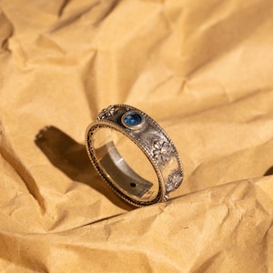 May include: A silver ring featuring a blue gemstone and floral details.