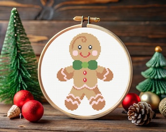 May include: A cross-stitch embroidery hoop with a white background and a gingerbread man design. The gingerbread man is brown with white icing and a green bow tie.