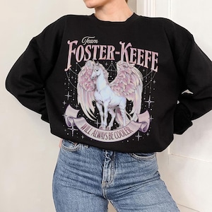 May include: Black sweatshirt with a pink and white unicorn with wings and the text "Team Foster-Keefe Will Always Be Cooler" printed on the front.