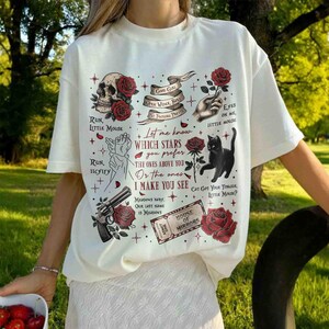 May include: White t-shirt with a black cat, red roses, and a skull graphic. The text on the shirt reads "Let me know which stars you prefer the ones above you or the ones I make you see".