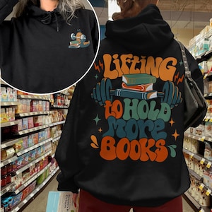 May include: Black hoodie with a graphic of a barbell with books on it and the text "Lifting to hold more books".