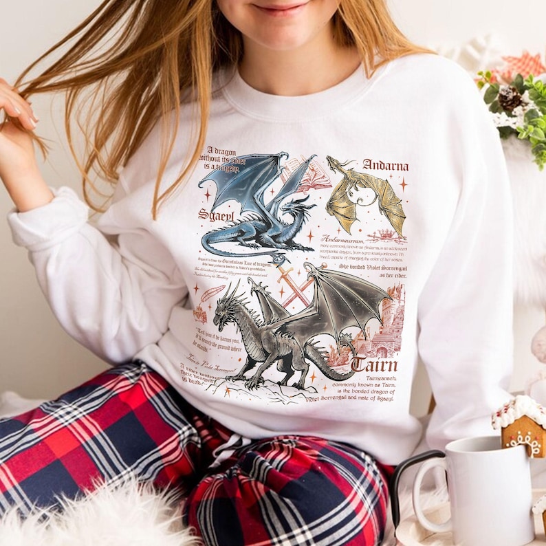 May include: White sweatshirt with a graphic print of three dragons with text that reads "A dragon without its rider is a fallen star", "Sgaepl", "Andarna", "Lairn", "Taimenect commonly known as Tairn, the bonded dragon of Sorrengal and of"