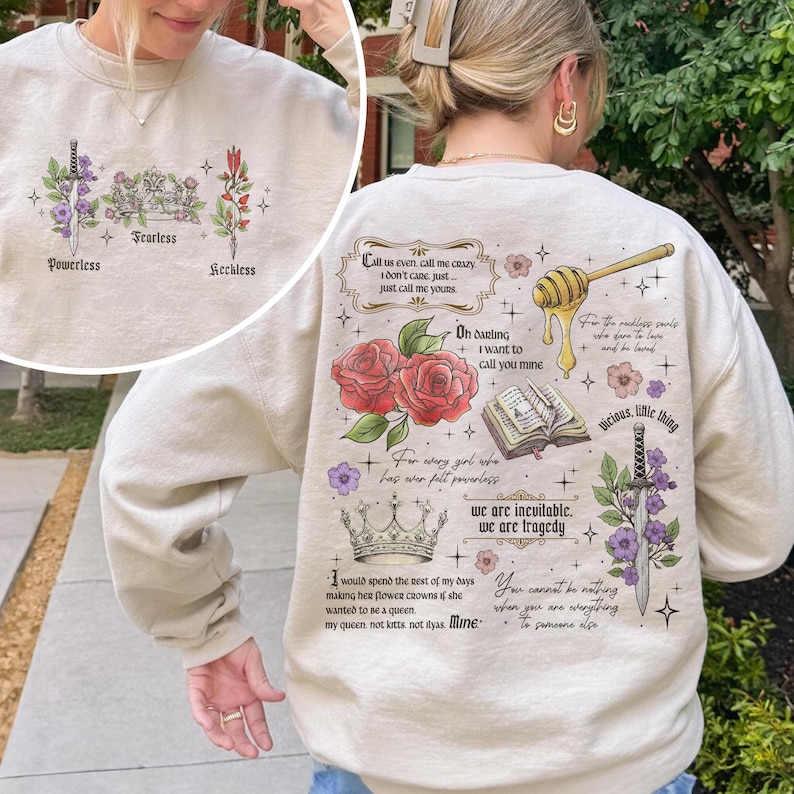 May include: A beige sweatshirt with a graphic print of flowers, crowns, swords, and text. The text includes quotes about love, power, and being a queen. The text reads: "Call us even call me crazy I don't care, just just call me yours. Oh darling I want to call you mine. For every girl who has ever felt powerless we are inevitable. We are tragedy. I would spend the rest of my days making her flower crowns if she wanted to be a queen. My queen, not kats, not ityas. Mine. You cannot be nothing when you are everything to someone else. Vicious, little thing."