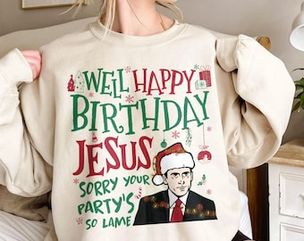 May include: A beige sweatshirt with a Christmas-themed graphic featuring a cartoon of a man wearing a Santa hat and the text "Well Happy Birthday Jesus Sorry Your Party's So Lame".