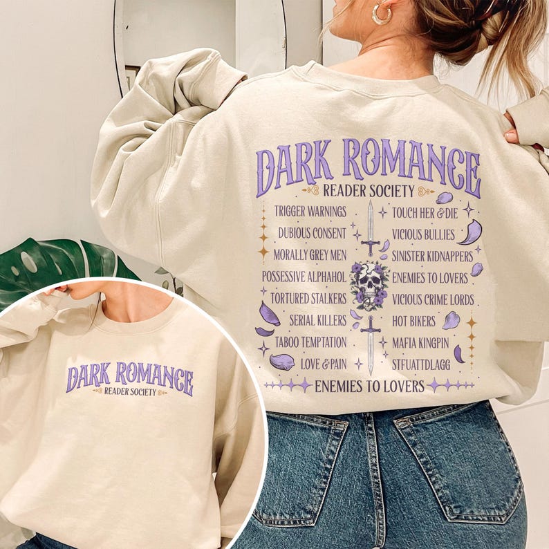 May include: A beige sweatshirt with the text "DARK ROMANCE READER SOCIETY" in purple. The back of the sweatshirt lists various romance novel tropes in a decorative layout, including "Trigger Warnings" and "Enemies to Lovers".