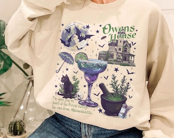 May include: A beige crewneck sweatshirt featuring a graphic print of a large house, a margarita glass, a black cat, a mortar and pestle, bats, and a moon. The text reads: Owens House and I'm sure you've heard of the Owens family. The ones from Massachusetts.