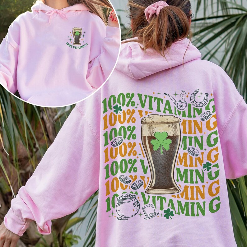 Puede incluir: Sudadera con capucha rosa claro con un dise&ntilde;o gr&aacute;fico en la parte delantera y trasera. La parte delantera muestra un vaso de cerveza con un tr&eacute;bol y el texto "100% Vitamin G". La parte trasera presenta un vaso de cerveza, una herradura y el texto "100% Vitamin G".
