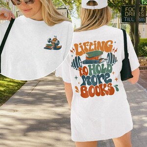 May include: White t-shirt with a graphic of a bookworm lifting weights with the text "Lifting to hold more books" on the back. The front of the shirt has a small graphic of a bookworm lifting a book.