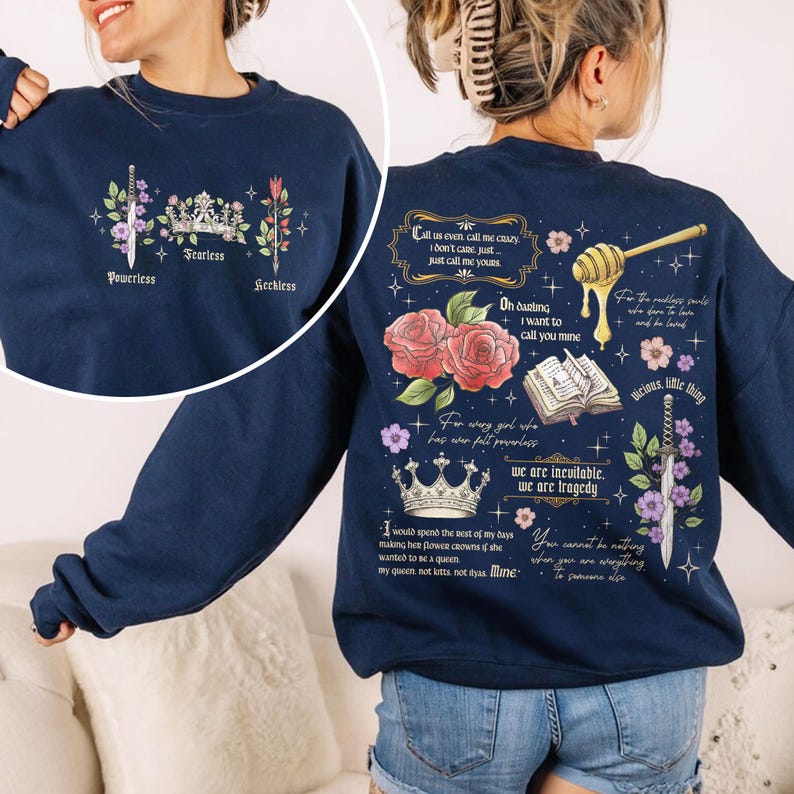 May include: Navy blue sweatshirt with a graphic print of flowers, crowns, swords, and text. The text includes quotes such as "Call us even, call me crazy, I don't care, just call me yours" and "For every girl who has ever felt powerless, we are invincible, we are tragedy".