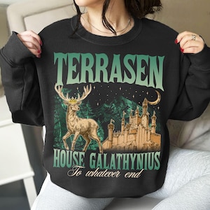 May include: Black sweatshirt with a graphic design featuring the word "TERRASEN" in green, a deer wearing a crown, a castle, and the text "HOUSE GALATHYNIUS To whatever end". The design has a fantasy theme.