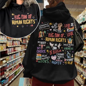 May include: A black hooded sweatshirt featuring a graphic print on the back with the text "BIG FAN OF HUMAN RIGHTS" surrounded by various icons and slogans including "FEMINISM IS FOR EVERYONE," "BLACK LIVES MATTER," and "LOVE IS LOVE."