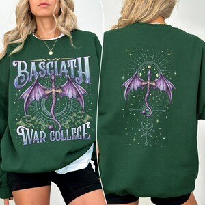 May include: Dark green sweatshirt with a front and back design. The front features the text "BASCIATH" above a purple dragon illustration, and "WAR COLLEGE" below. The back has a similar dragon design. The sweatshirt has a crew neck.