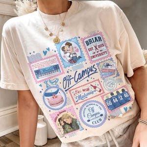 May include: A cream-colored short-sleeve t-shirt featuring a collage of colorful graphic illustrations, including a couple embracing, a keyboard, a stack of books, a pizza slice, a burger, a bottle, and hockey jerseys with the numbers 66, 44, 22, and 46.